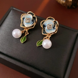 Detailed close-up of gold flower earrings with blue enamel, zircon, and pearls