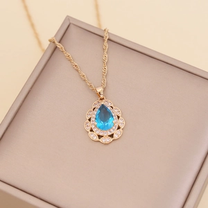 Detailed close-up of a pear-shaped blue gemstone pendant on a gold twisted chain necklace