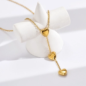 Collier en acier inoxydable plaqué or 18k avec trois cœurs suspendus sur support blanc
