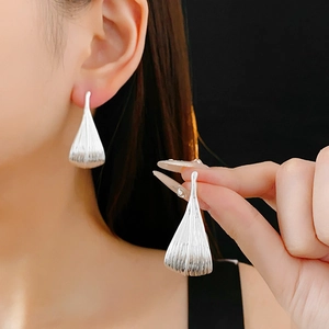 Detailed close-up of silver-plated ginkgo leaf earrings worn by a model against dark wall