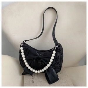Detail of black textured shoulder bag featuring large bow and decorative pearl handle chain