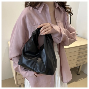 Close-up of a black pleated leather cloud bag held by a model in a minimalist setting