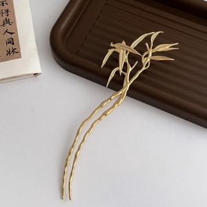 Detailed view of a golden bamboo-shaped metal hair stick with tassel on a zen tray
