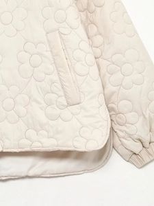 Detail of floral quilted texture on beige jacket showing side pocket and ribbed cuffs