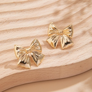 Close-up of golden bow-knot earrings with vintage metallic texture on wooden display