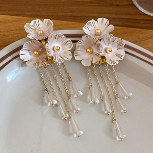Detailaufnahme eleganter Blumenohrringe mit weißen Harzblüten und goldenen Kettenquasten