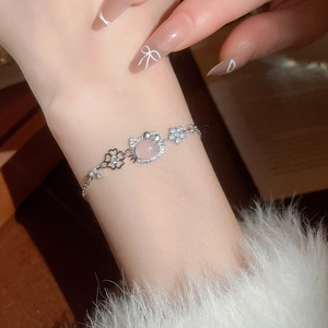 Detail of pink heart-shaped cat opal pendant on silver bracelet with floral charms