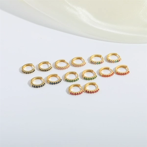 Set of seven pairs of gold-plated huggie earrings with colorful zircon stones on white fabric