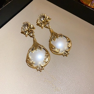 Close-up of matte gold flower and teardrop frame earrings with white pearls and rhinestones