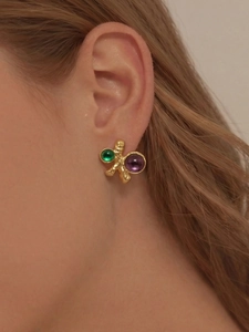 Gros plan de boucles d'oreilles dorées avec pierres vertes et violettes sur un mannequin