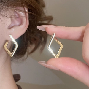 Detail view of geometric diamond-shaped gold earrings worn by a model in warm light