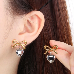 Detail of bowknot stud with silver heart pendant on gold plated stainless steel earring