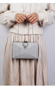 Detail view of silver evening clutch bag featuring leaf-shaped metal clasp and chain strap