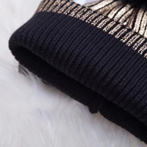 Women's warm winter knit beanie in black with elegant gold stripe and pompom detail