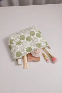 Detail of white cotton linen makeup bag featuring green leaf embroidery and zipper