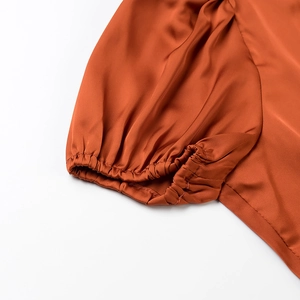 Gros plan détaillé de la manche bouffante en satin marron-orangé à poignet élastique