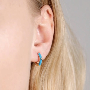 Detailed macro view of light blue enamel heart earring with gold finish on ear lobe