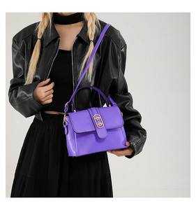 Detail of vibrant purple crossbody bag with gold hardware worn over a black leather jacket