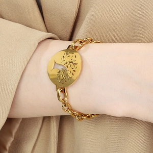 Golden link bracelet with hollow peacock charm worn on wrist against a beige blazer
