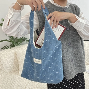 Détail d'un sac cabas en jean bleu avec motifs de nœuds blancs et livres à l'intérieur