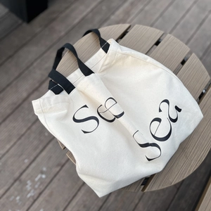 Off-white canvas tote bag with black letter print on a rustic wooden table surface