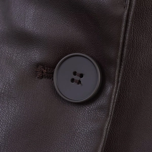 Detail der dunkelbraunen Lederstruktur und eines matten Vierlochknopfes am Blazer