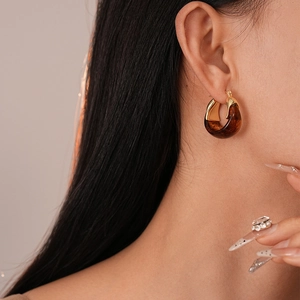 Nahaufnahme eines Models mit bernsteinfarbenen Harz-Creolen mit goldenem Metallfinish