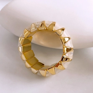 Detailed close-up of geometric gold and white faceted elastic ring on a white stone