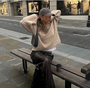 Look urbain avec un pull en maille beige, un pantalon en cuir noir et une casquette