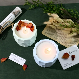 Top view of lit scented candles with dried flower petals in geometric textured jars