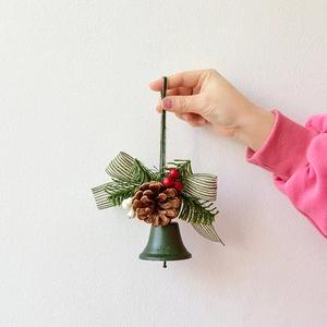 Green metal Christmas bell hanging ornament with pine cones berries and striped bow