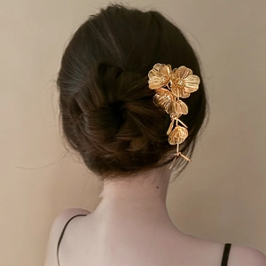 Elegant gold hollow flower hair pin accessory shown on dark hair with soft lighting
