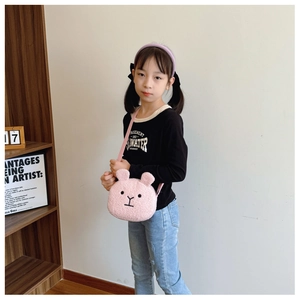 Close-up of pink plush rabbit shoulder bag worn by a young child in a cozy home setting
