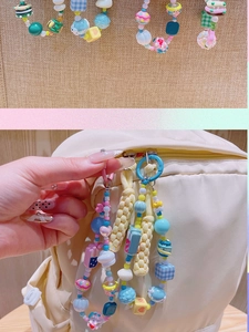 Détail d'une dragonne de téléphone en perles pastel avec breloques sur un sac à dos
