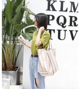 Vertical striped beige canvas tote bag shown worn by a model in a bright outdoor setting