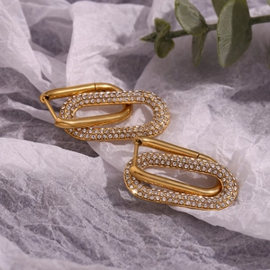 Detail of gold double oval earrings with micro-set zircons on textured white paper