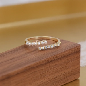 Macro detail of 14k gold-plated open ring featuring crisscross pearls and zircon crystals