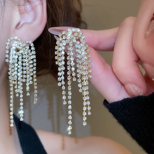 Close-up of sparkling gold tassel earrings with rhinestone fringe worn by a model