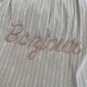 Detail of the Bonjour embroidered text on the striped khaki canvas tote bag fabric