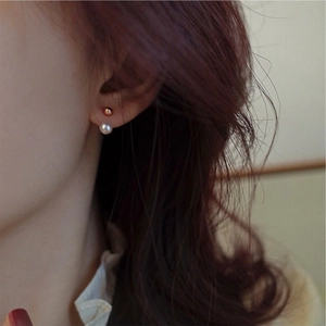 Minimalist gold ball and freshwater pearl stud earrings shown on model ear for women