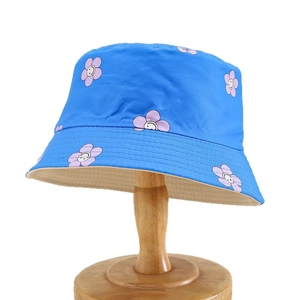 Blue reversible sun hat for girls with smiling flower pattern on a wooden head stand