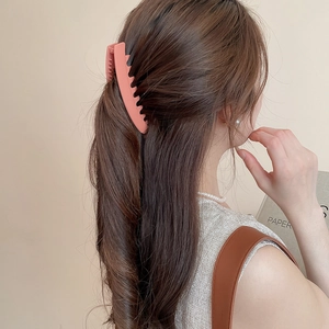 Détail d'une barrette banane en acrylique rose mat portée en queue de cheval pour femme