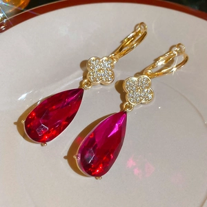 Close-up of gold drop earrings featuring a diamond clover and red pear-shaped gemstone