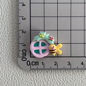 Détail d'une breloque en résine abeille et fleur sur une règle mesurant environ 2 cm