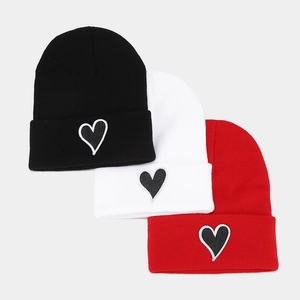 Trois bonnets en tricot noir, blanc et rouge avec écussons en cœur brodés