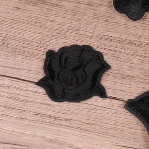 Black rose embroidery patch for clothing repair on a rustic wooden background