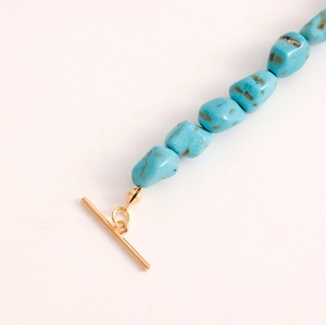 Detail of irregular turquoise beads with a gold T-bar toggle clasp on a white background