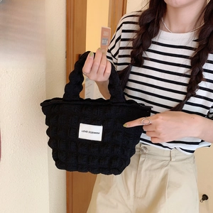 Detail view of black quilted bubble texture tote bag with white logo label and zipper