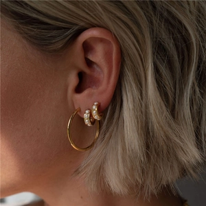 Close-up of gold hoop and pearl huggie earrings styled together on a female model