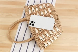 Detailed macro view of woven straw tote bag texture beside a phone for size reference
